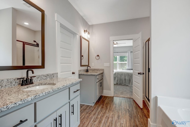 bathroom featuring ceiling fan, hardwood / wood-style floors, a tub to relax in, and dual bowl vanity