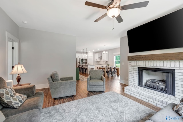 living room with a fireplace, ceiling fan with notable chandelier, and wood-type flooring