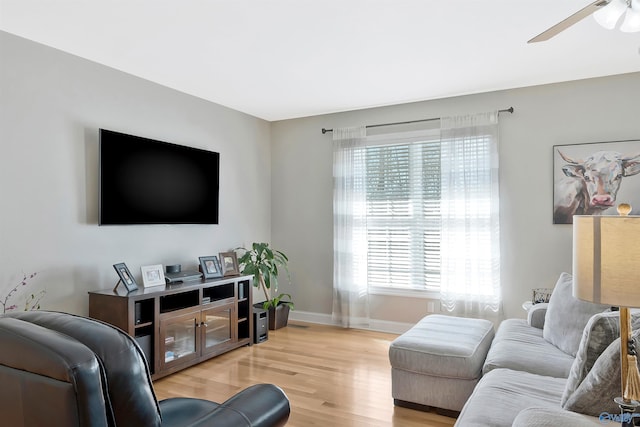 living room featuring baseboards, light wood-type flooring, and a ceiling fan