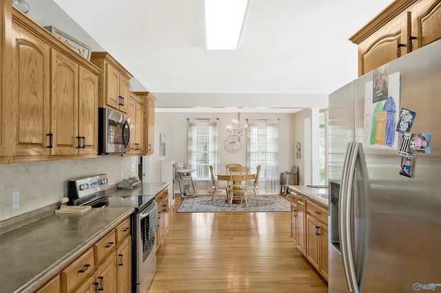 kitchen featuring an inviting chandelier, stainless steel appliances, decorative backsplash, light wood-style flooring, and hanging light fixtures