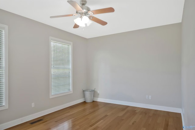 unfurnished room featuring baseboards, visible vents, wood finished floors, and a healthy amount of sunlight