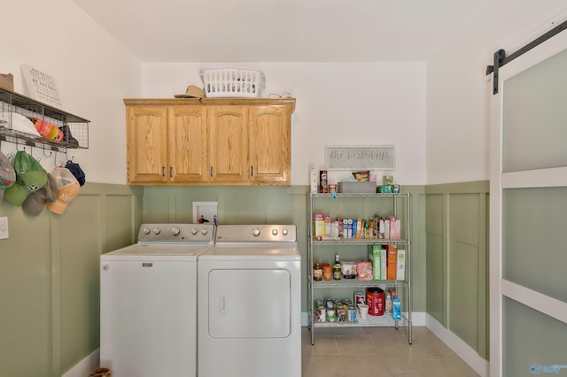 laundry area with light tile patterned floors, washing machine and dryer, a barn door, a wainscoted wall, and cabinet space