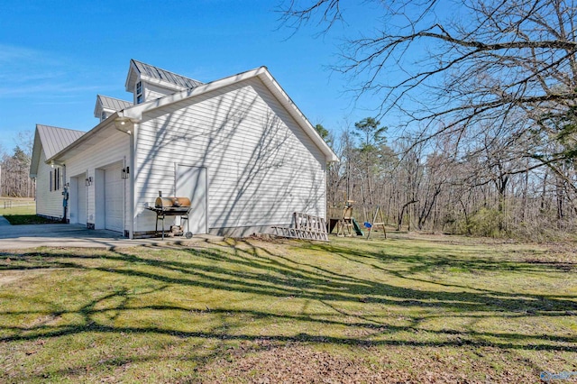 view of side of property featuring a garage, concrete driveway, metal roof, and a lawn