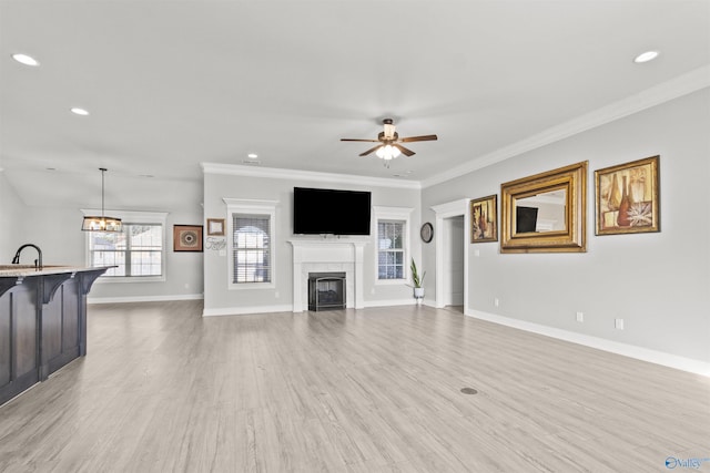 unfurnished living room with a tile fireplace, sink, light wood-type flooring, ceiling fan with notable chandelier, and ornamental molding