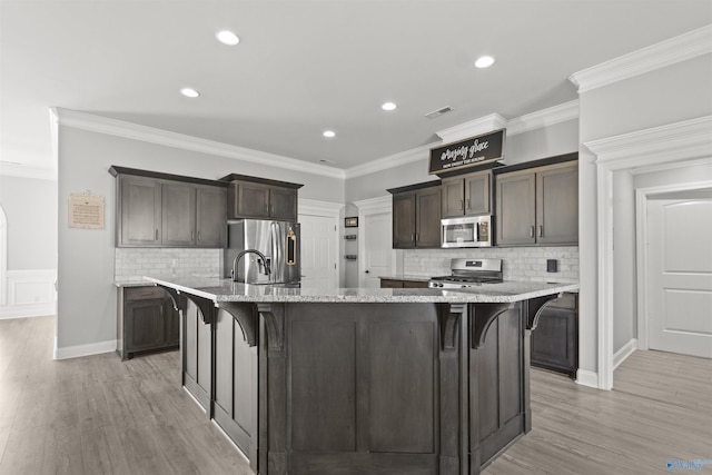 kitchen featuring an island with sink, stainless steel appliances, light wood-type flooring, and ornamental molding