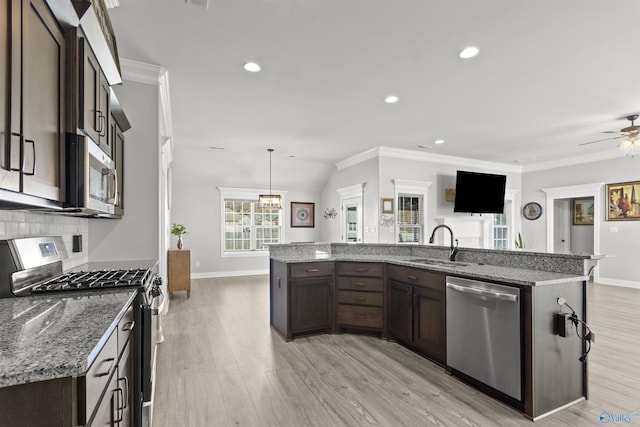 kitchen with a kitchen island with sink, hanging light fixtures, light wood-type flooring, light stone countertops, and stainless steel appliances