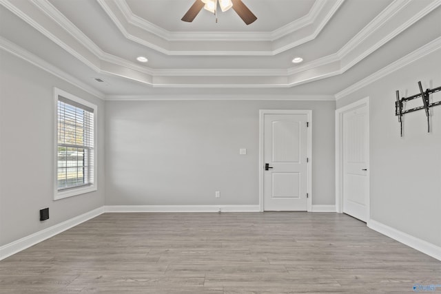 spare room featuring light wood-type flooring, a raised ceiling, ceiling fan, and ornamental molding