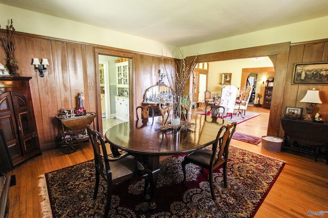 dining area featuring wood finished floors, arched walkways, and wood walls