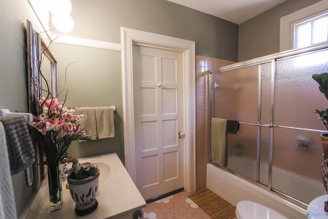 full bath with combined bath / shower with glass door, toilet, vanity, and tile patterned floors