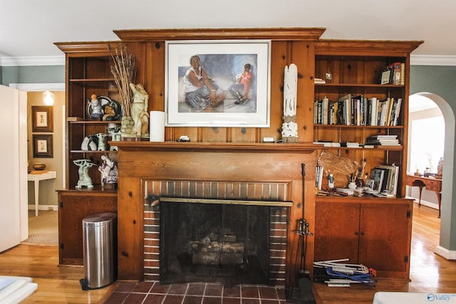 interior details with arched walkways, a fireplace, crown molding, and wood finished floors