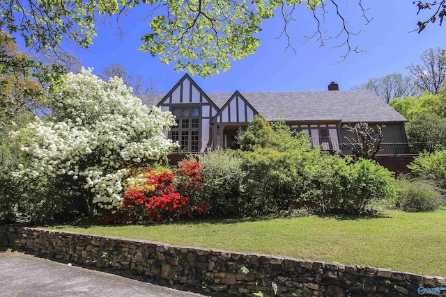 tudor house featuring stucco siding, a chimney, a front lawn, and a shingled roof