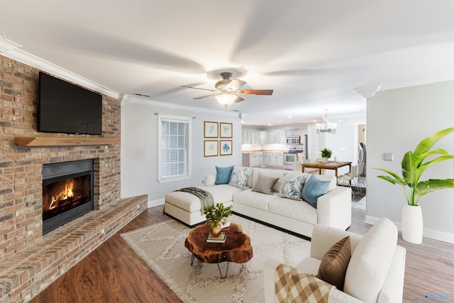 living room with a fireplace, wood finished floors, ornamental molding, and ceiling fan with notable chandelier