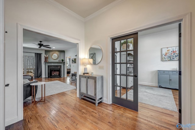 interior space featuring crown molding, ceiling fan, baseboards, a fireplace, and wood finished floors