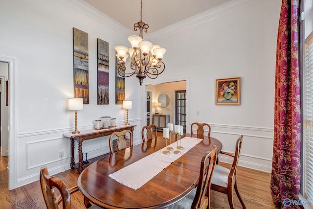 dining space with wood finished floors, a wainscoted wall, ornamental molding, a decorative wall, and a notable chandelier