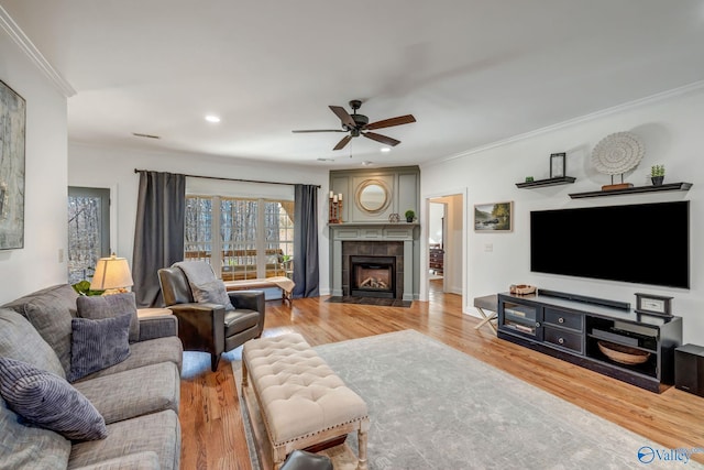 living room featuring a tiled fireplace, crown molding, wood finished floors, and a ceiling fan