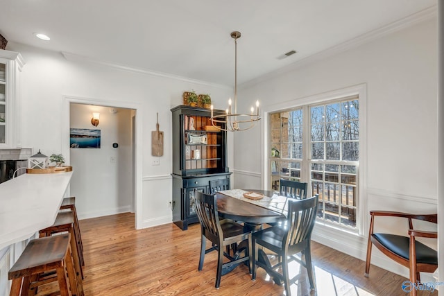 dining area featuring baseboards, visible vents, light wood finished floors, an inviting chandelier, and ornamental molding