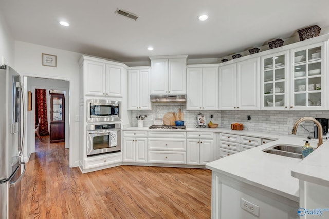 kitchen with visible vents, a sink, under cabinet range hood, white cabinetry, and appliances with stainless steel finishes