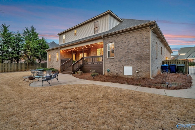 back of property at dusk with brick siding, a patio area, a yard, and fence