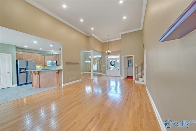 unfurnished living room with a high ceiling, a chandelier, light hardwood / wood-style flooring, and ornamental molding