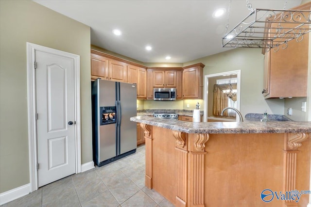 kitchen with stainless steel appliances, sink, kitchen peninsula, light brown cabinetry, and a notable chandelier