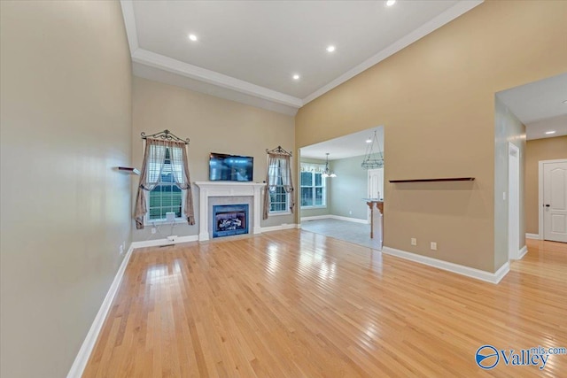 unfurnished living room featuring a high ceiling, a chandelier, light wood-type flooring, and crown molding