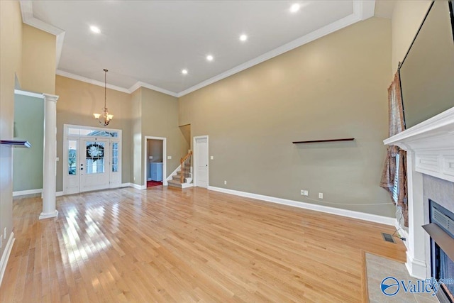 unfurnished living room featuring an inviting chandelier, a premium fireplace, ornamental molding, light wood-type flooring, and a high ceiling