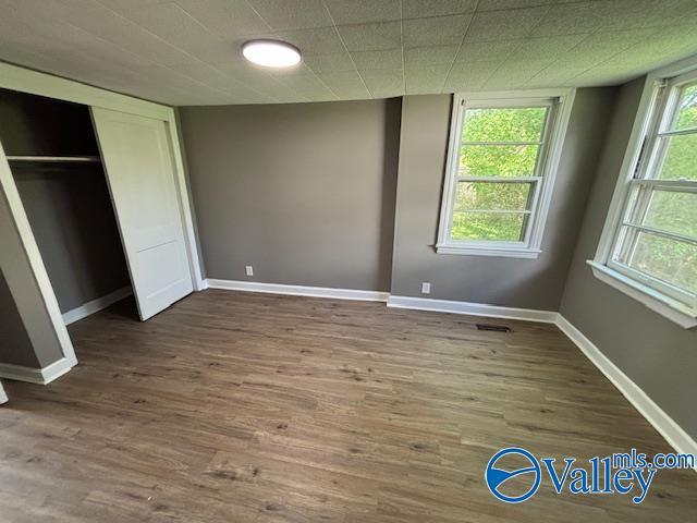 unfurnished bedroom with wood finished floors, baseboards, a closet, and visible vents