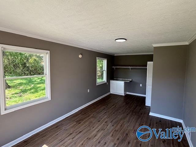 unfurnished bedroom featuring a textured ceiling, baseboards, crown molding, and wood finished floors