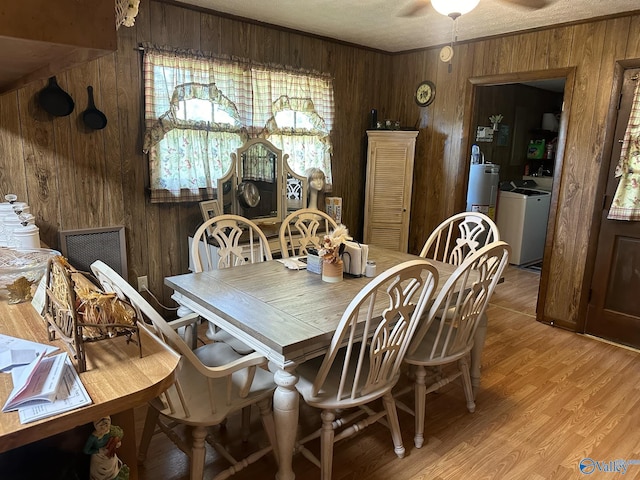 dining area featuring light wood-type flooring, wood walls, separate washer and dryer, water heater, and ceiling fan