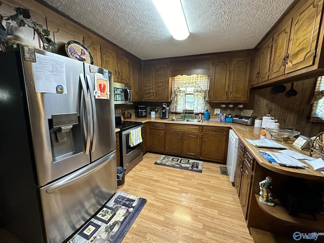 kitchen with a textured ceiling, stainless steel appliances, sink, and light hardwood / wood-style floors