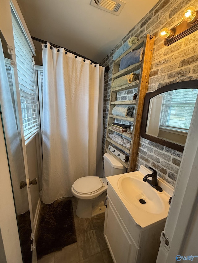 bathroom with toilet, brick wall, vanity, and visible vents