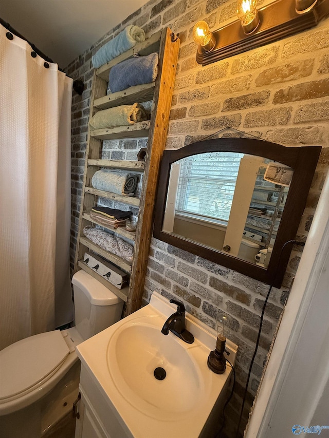 bathroom with toilet, brick wall, and vanity