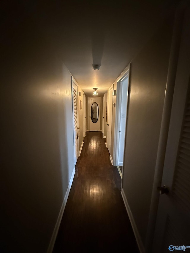 corridor with dark wood-style flooring and baseboards