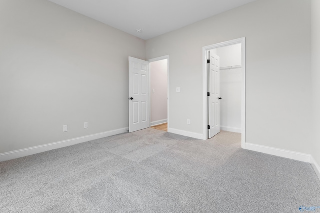 unfurnished bedroom featuring baseboards, light carpet, and a walk in closet