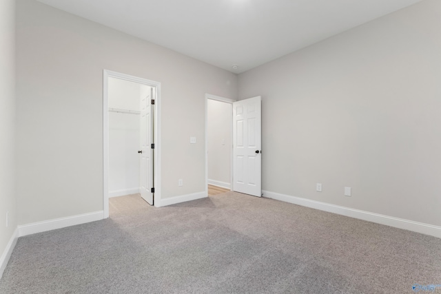 unfurnished bedroom with a spacious closet, light colored carpet, and baseboards