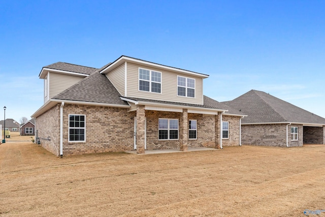 view of front facade with a front lawn, a patio area, brick siding, and roof with shingles