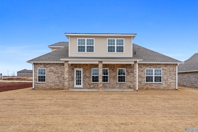 back of property with a yard, a patio, brick siding, and a shingled roof