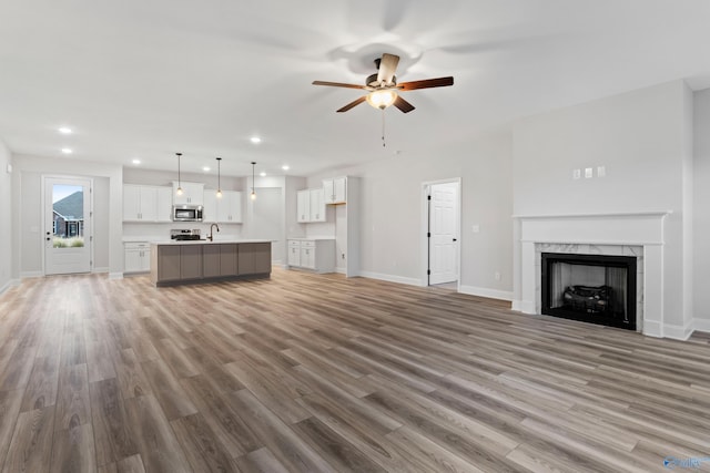 unfurnished living room featuring light wood finished floors, baseboards, a premium fireplace, recessed lighting, and a sink