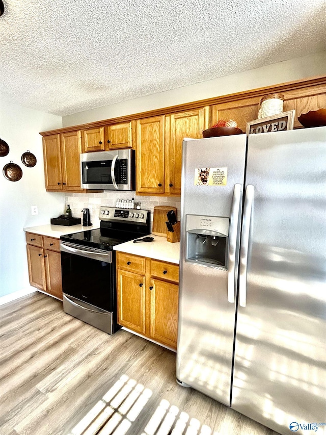 kitchen featuring tasteful backsplash, appliances with stainless steel finishes, light hardwood / wood-style floors, and a textured ceiling