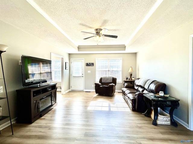 living room with light wood-type flooring, a textured ceiling, ceiling fan, and a tray ceiling