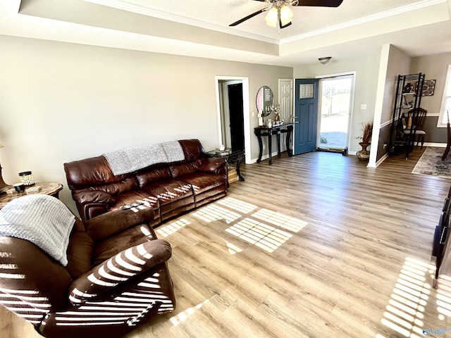 living room with crown molding, hardwood / wood-style flooring, a raised ceiling, and ceiling fan