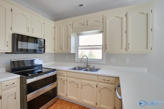 kitchen with light hardwood / wood-style flooring, cream cabinets, sink, and stainless steel range with electric cooktop