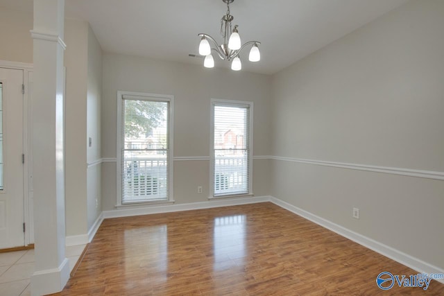 unfurnished dining area featuring a chandelier, ornate columns, and light wood-type flooring