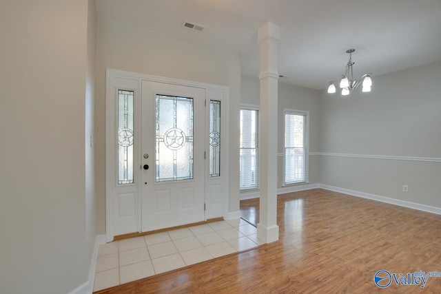 foyer featuring light hardwood / wood-style floors, a notable chandelier, and decorative columns