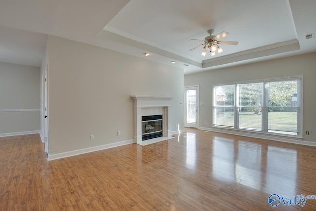 unfurnished living room featuring light hardwood / wood-style flooring, a tile fireplace, and a tray ceiling