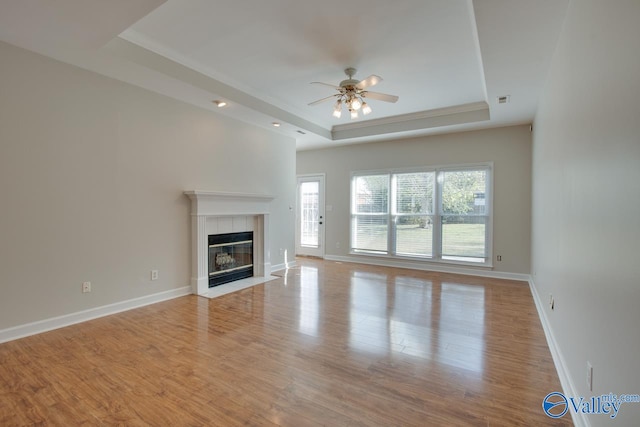 unfurnished living room with ceiling fan, a tile fireplace, light hardwood / wood-style flooring, and a tray ceiling