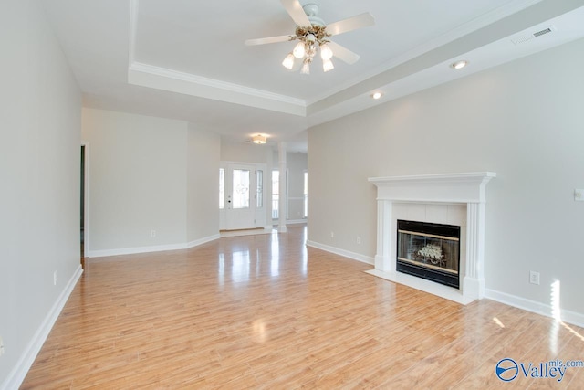 unfurnished living room with ornamental molding, light wood-type flooring, a tray ceiling, and ceiling fan