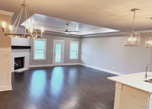 unfurnished living room featuring a tray ceiling, dark wood-type flooring, ornamental molding, and ceiling fan with notable chandelier