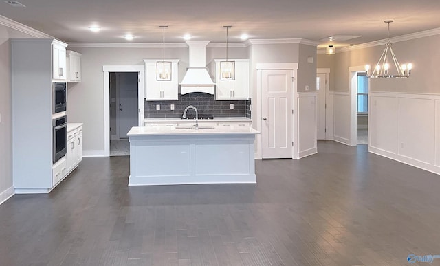 kitchen with hanging light fixtures, white cabinets, a center island with sink, custom exhaust hood, and oven