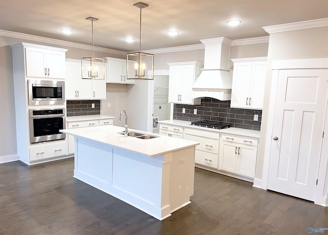 kitchen with appliances with stainless steel finishes, custom range hood, a center island with sink, and white cabinets